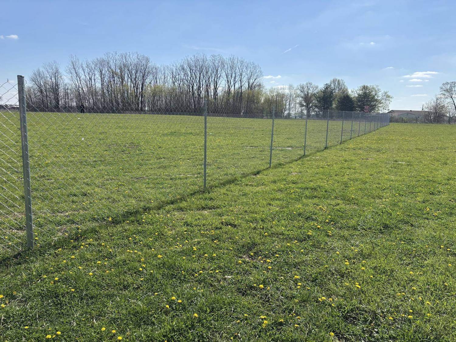 A post driven temporary chain link fence running the length of a grass field, with the posts set straight into the ground