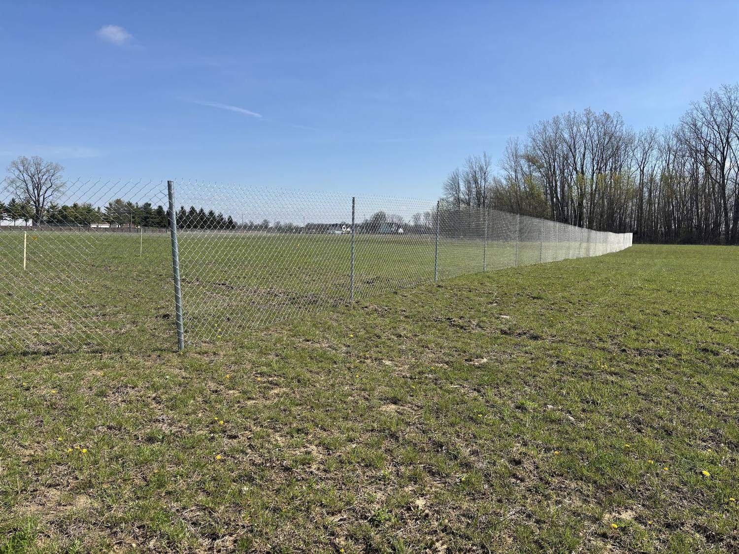 A long run of post driven temporary chain link fence across open ground, posts driven in with the fabric tensioned on them